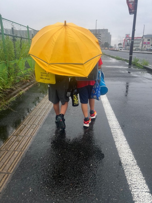 雨の日、ひとつの傘で帰る子どもたちの後ろ姿