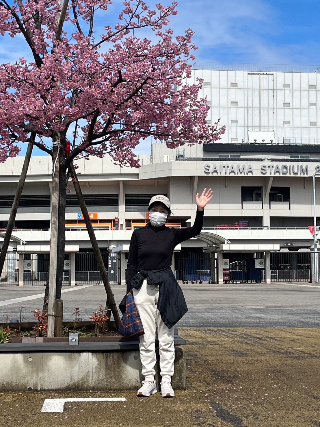 くみこ先生(桜の木の横で手を上げている写真)
